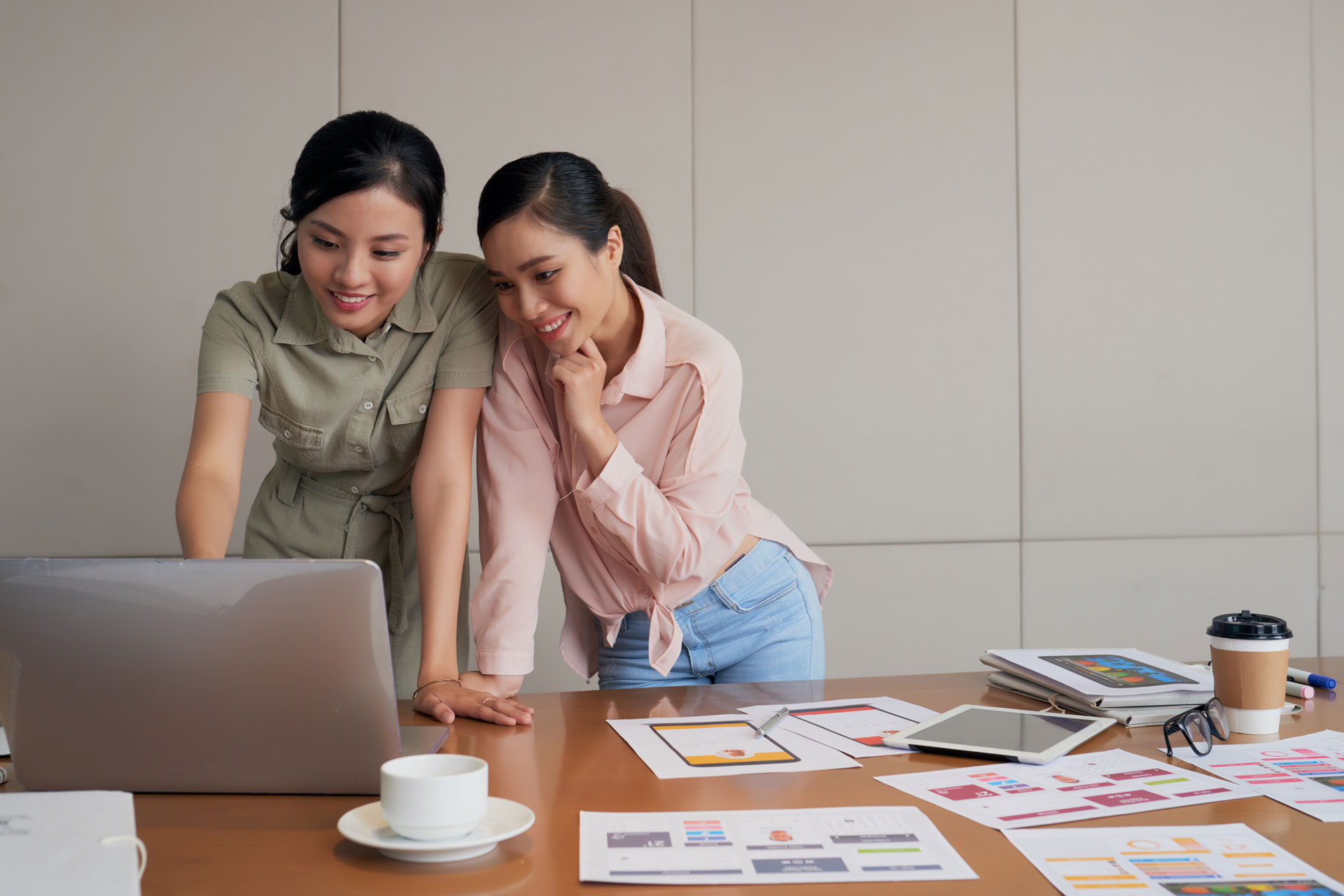 two-young-asian-female-coworkers-standing-desk-using-laptop